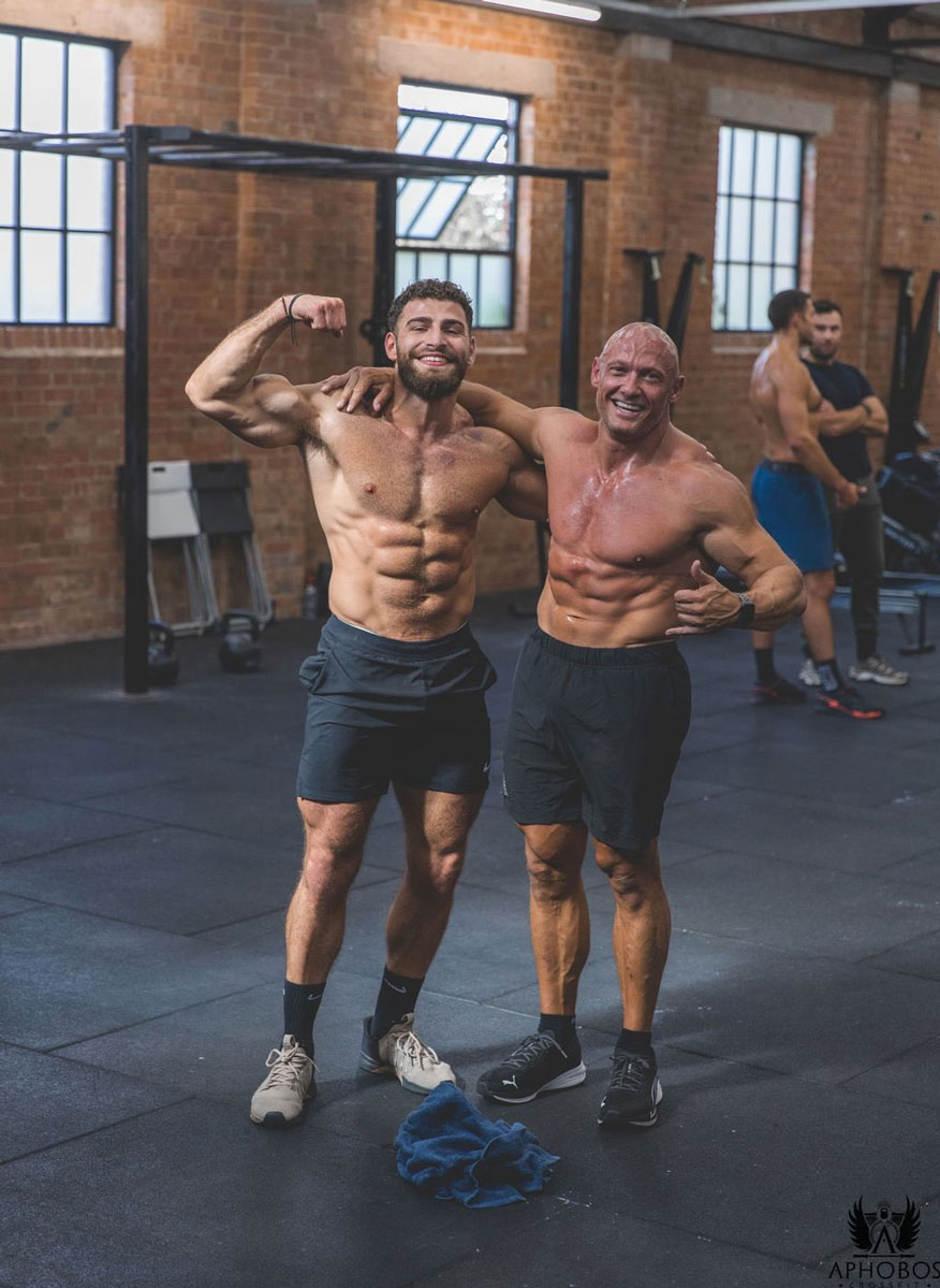 Coach is posing with one other person in the gym.